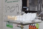 Spülmaschine mit Geschirr. Im Hintergrund Werbeaufdrucke auf Containern.